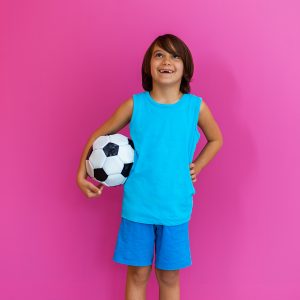 Portrait of young Arabic boy with soccer ball isolated against pink background and copy space